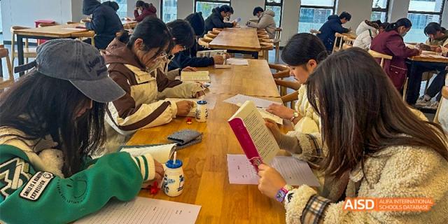 Students sit at a long wooden table in a library, silently reading books and taking notes during study hour. Hefei No.8 High School.