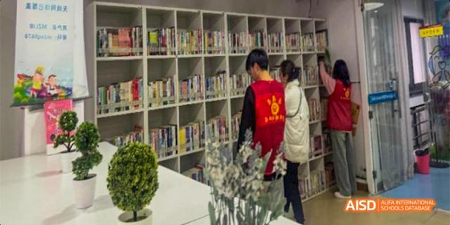 Students in red volunteer vests assist in organizing a large collection of books on tall white library shelves. Hefei No.8 High School.