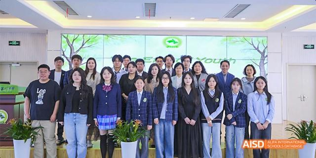 A large group of faculty and students pose for a formal commemorative group photo in front of a green backdrop. Hefei No.8 High School.