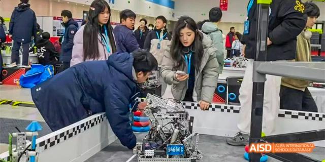 Students gather around a robotics competition area, adjusting a complex mechanical robot on a checkered track. Hefei No.8 High School.