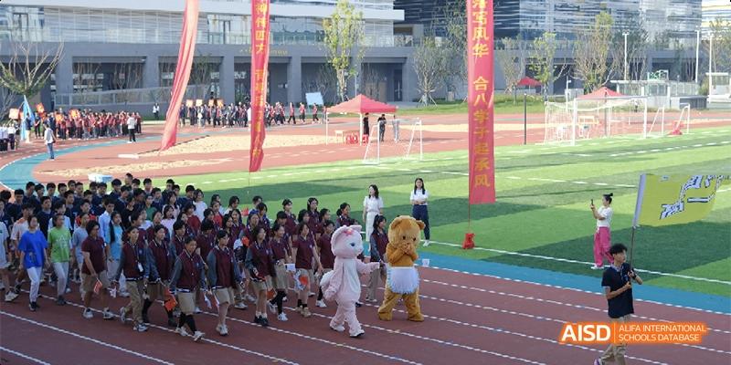 Students and mascots march together during a sports ceremony on a large outdoor field at Hefei No.8 High School.