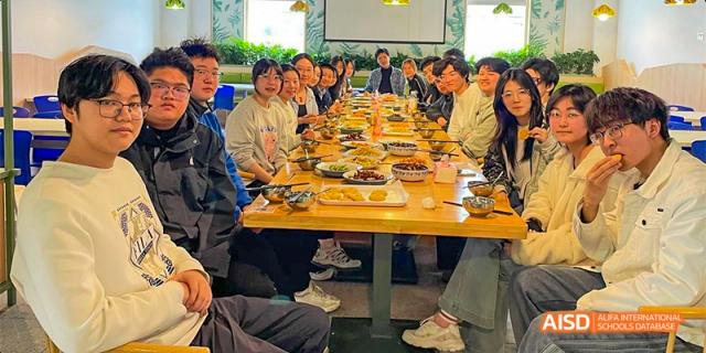 Students sitting at a long wooden table filled with various dishes during a group meal at Hefei No.8 High School.