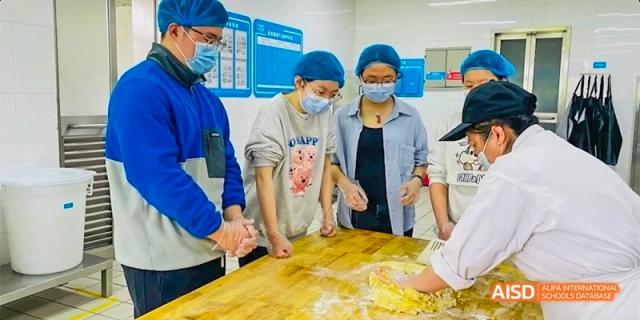 Students wearing hairnets and masks gathered around a table to prepare dough at Hefei No.8 High School.