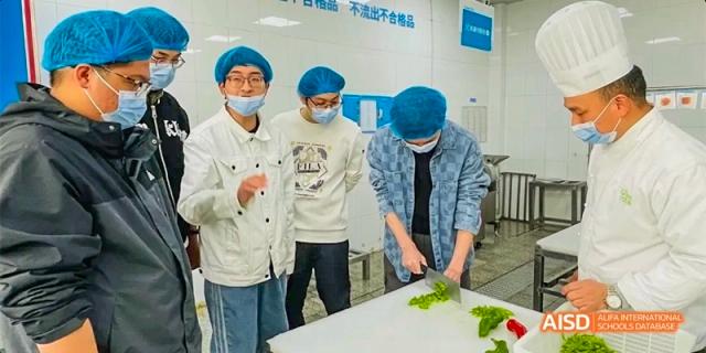 Students in a kitchen setting watching a classmate practice vegetable chopping at Hefei No.8 High School.