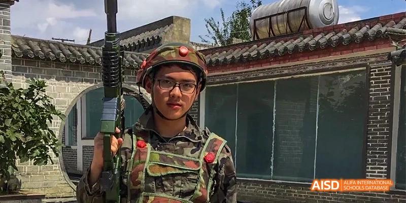 A male student from Kunming No.1 High School International Education poses for a photo, wearing glasses and a camouflage vest.