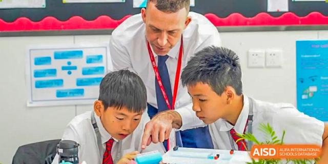 A teacher from Lady Eleanor Holles International School Foshan (LEH Foshan) helps two students with a project, pointing at a book.