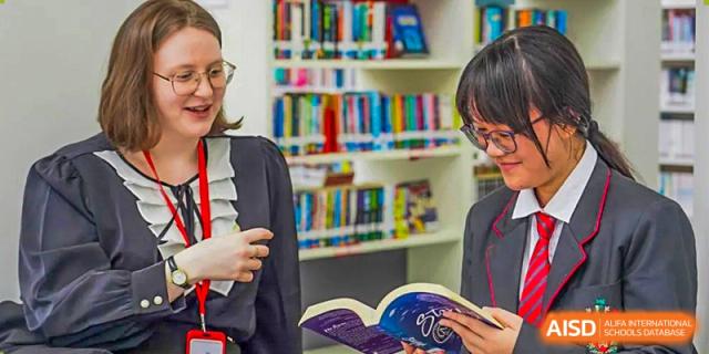 Two students from Lady Eleanor Holles International School Foshan (LEH Foshan) stand in a library, looking at books on the shelves.