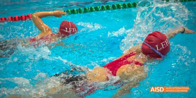 A swimmer in a red swimsuit at Lady Eleanor Holles International School Foshan (LEH Foshan) racing in a bright blue swimming pool, with a red buoy nearby.