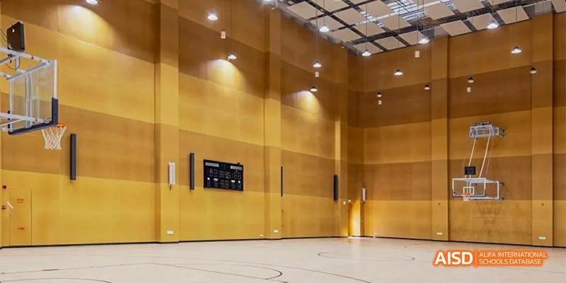 An indoor gymnasium at Lady Eleanor Holles International School Foshan (LEH Foshan), featuring wooden walls, a scoreboard, and bright overhead lights.