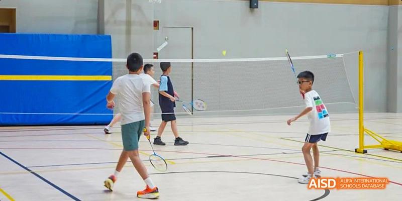 Two students from Lady Eleanor Holles International School Foshan (LEH Foshan) playing badminton in a well-lit indoor gymnasium.