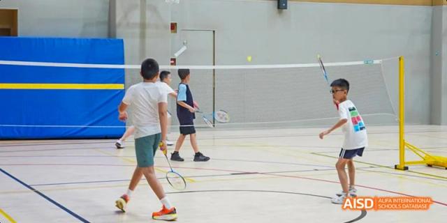 Two students from Lady Eleanor Holles International School Foshan (LEH Foshan) playing badminton in a well-lit indoor gymnasium.