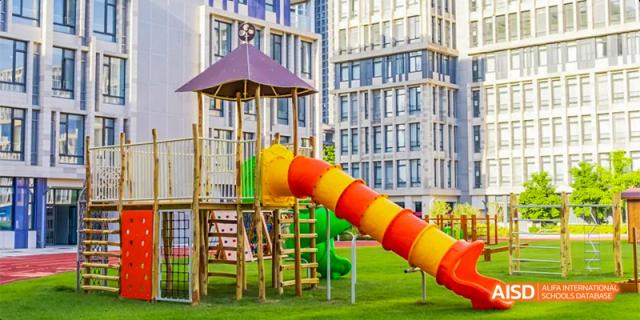A colorful playground with a yellow and red slide in front of the modern school building at Lady Eleanor Holles International School Foshan(LEH Foshan).