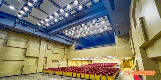 An auditorium at Lady Eleanor Holles International School Foshan(LEH Foshan) with rows of red seats, a stage, and bright overhead lights.