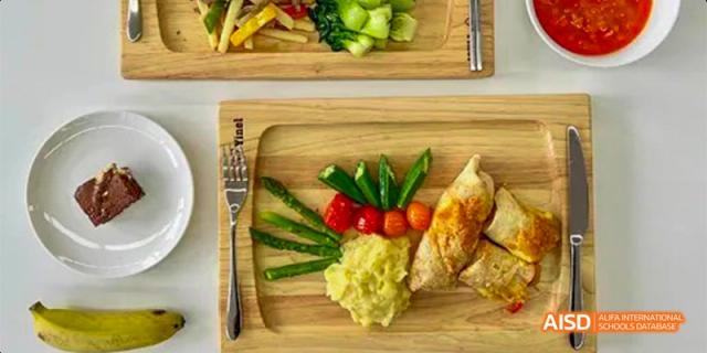 A prepared meal on a wooden board from Lady Eleanor Holles International School Foshan(LEH Foshan), featuring mashed potatoes, asparagus, tomatoes, and fried chicken.
