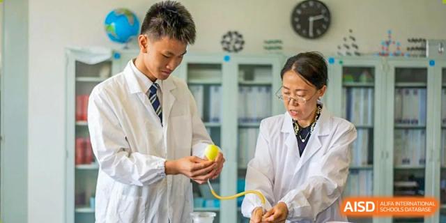 Students from Nord Anglia School Guangzhou Panyu wearing lab coats and safety glasses, working together on a hands-on science project.
