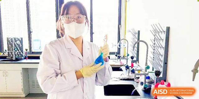 A student from Nord Anglia School Guangzhou Panyu wearing a lab coat and gloves, holding a beaker during a science experiment.