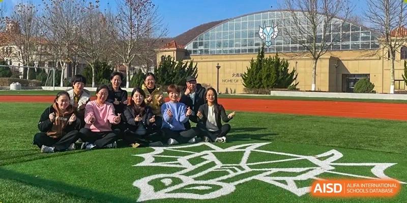 Group photo of Nord Anglia School Guangzhou Panyu students and teachers on a sports field with the school building in the background.