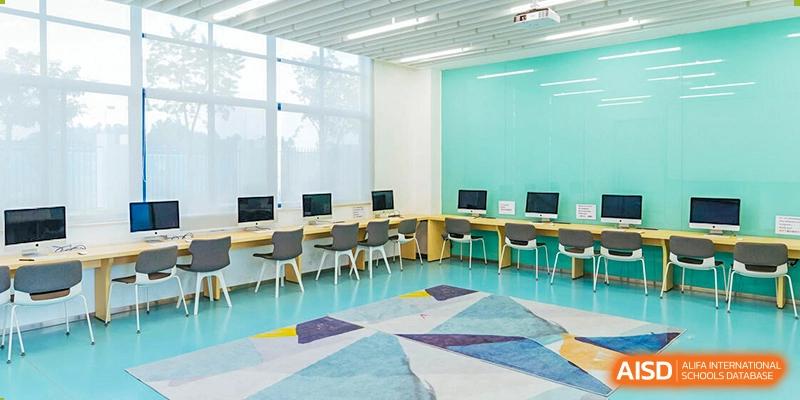 A bright, colorful classroom at Nord Anglia School Guangzhou Panyu with a turquoise wall, computers, and tables.