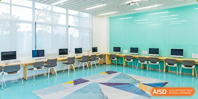 A bright, colorful classroom at Nord Anglia School Guangzhou Panyu with a turquoise wall, computers, and tables.