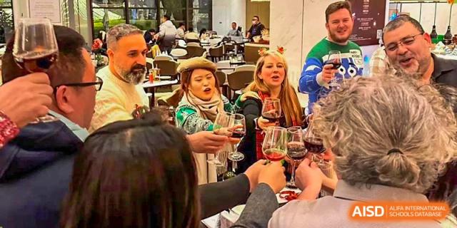 Two people from Nord Anglia School Guangzhou Panyu toasting with glasses of red wine at a social gathering.