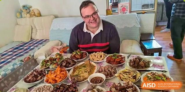 A group of friends or family enjoying a meal with several large dishes, possibly at an event for Nord Anglia School Guangzhou Panyu.