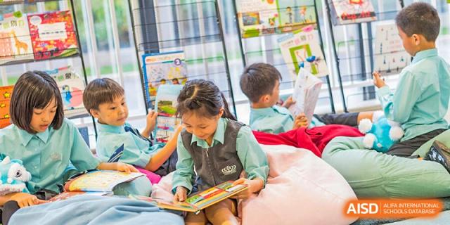 A young girl in a school uniform from Nord Anglia School Guangzhou Panyu reading a book while a boy looks on in the background.