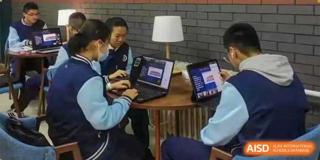 Two students working collaboratively on laptops at a small table with a lamp, studying late at Orange County American High School Beijing Campus.