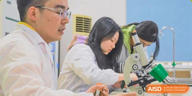 A female student in a lab coat working on a science experiment or project under the supervision of a teacher at Orange County American High School Beijing Campus.