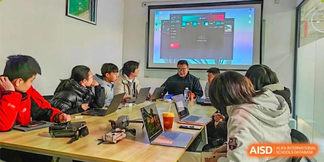 A small group of students and a teacher having a focused discussion around a table with laptops at Orange County American High School Beijing Campus.