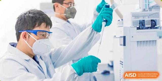 A close-up of a person in a lab coat and green gloves using a pipette in a science laboratory at Orange County American High School Beijing Campus.