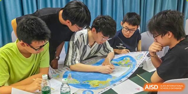 Students gathered around a table studying a large world map during a geography or history class at Orange County American High School Beijing Campus.
