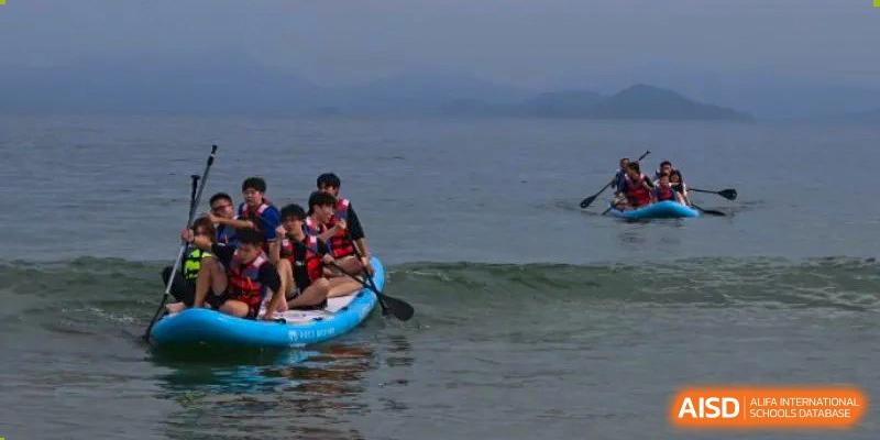 Students paddleboarding or kayaking on the water near a shore, with one student holding a paddle, at Orange County American High School Beijing Campus.