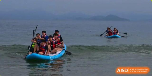 Students paddleboarding or kayaking on the water near a shore, with one student holding a paddle, at Orange County American High School Beijing Campus.