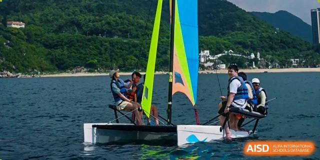 Students sailing or windsurfing on the water with colorful sails, as part of an outdoor activity at Orange County American High School Beijing Campus.