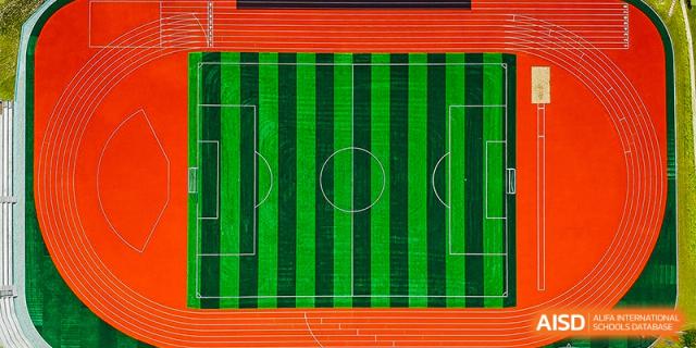 An aerial view of the vibrant green and orange soccer field and running track at Oriental Cambridge International School.