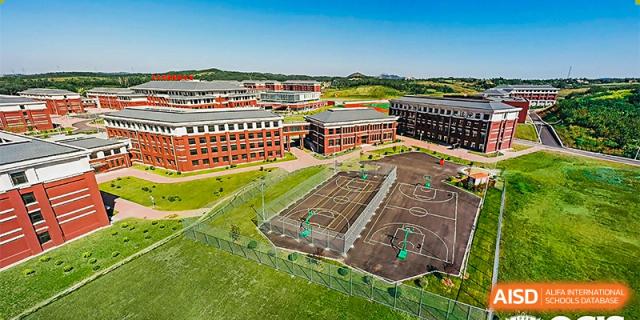 An aerial view of the sports facilities at Oriental Cambridge International School, including the basketball courts and surrounding red brick school buildings.