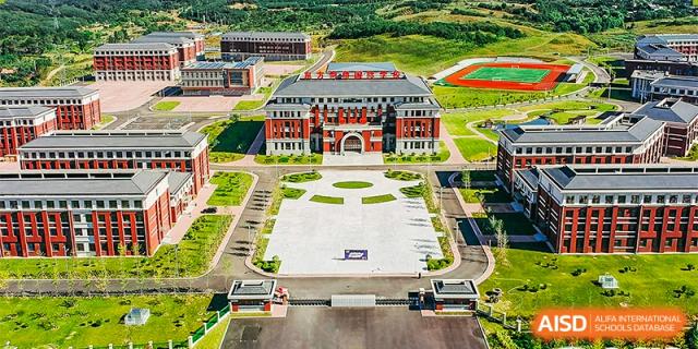 A close aerial shot focusing on the impressive front entrance and main academic buildings of Oriental Cambridge International School, with a large, paved assembly area.