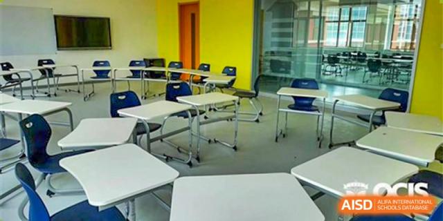 A brightly colored classroom at Oriental Cambridge International School with modular white desks and yellow chairs against a blue and yellow wall.