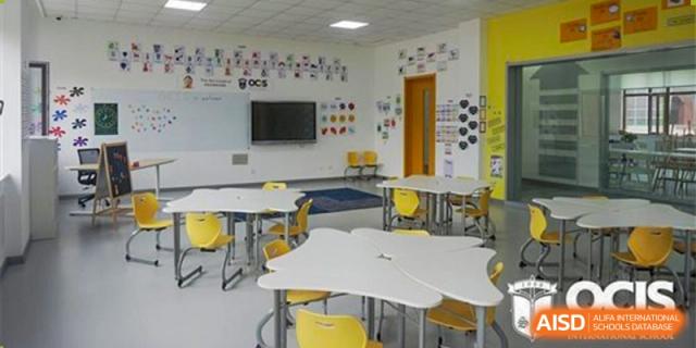 An interior photo of a modern classroom at Oriental Cambridge International School, featuring yellow chairs and modular, triangular white desks.