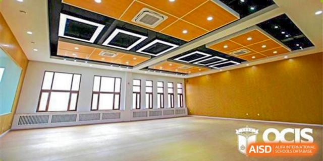 An empty multi-purpose room at Oriental Cambridge International School with high windows, wood paneling, and an orange ceiling with a modern lighting design in the center.