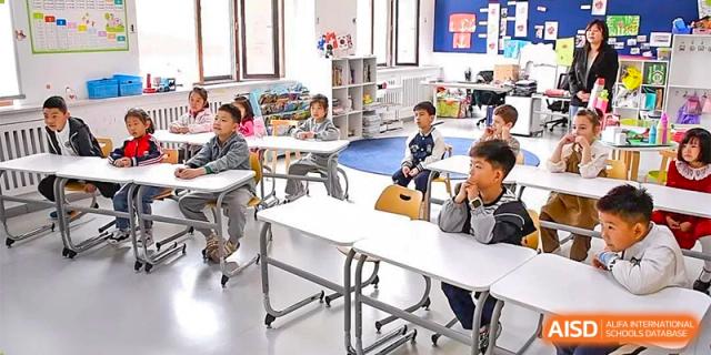 Students at Oriental Cambridge International School seated at white modular desks in a classroom, attentively looking toward the front.