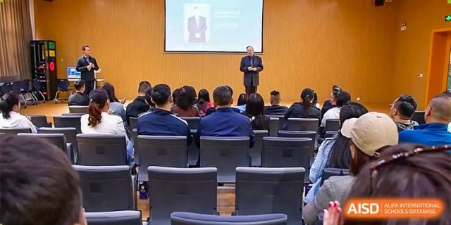 An audience of adults and students at Oriental Cambridge International School seated in a lecture hall, facing a speaker or presentation on a stage.