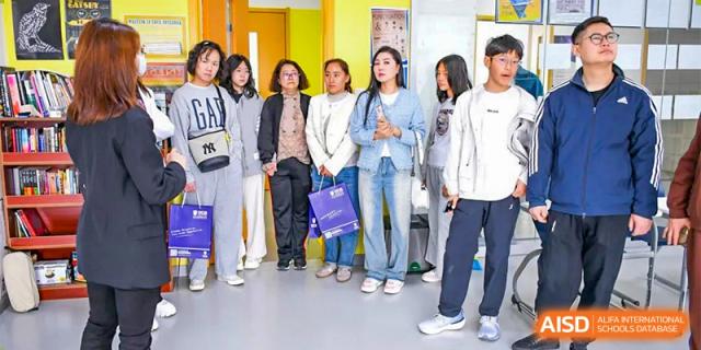A group of adults or staff from Oriental Cambridge International School standing and waiting in a line in a hallway, some holding bags.