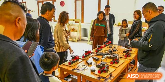 An activity at Oriental Cambridge International School where an instructor is showing a group of students how to work with small electronic components and wires on a wooden table.