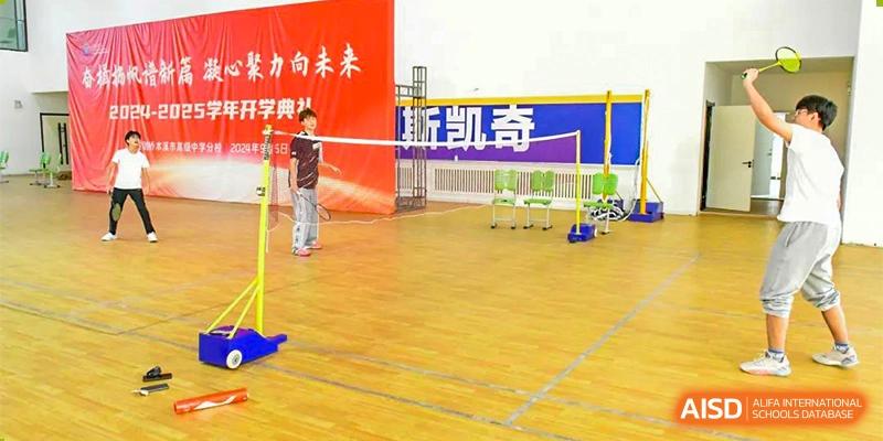 The indoor sports hall at Oriental Cambridge International School set up for badminton, showing a student near the net on the wooden court.