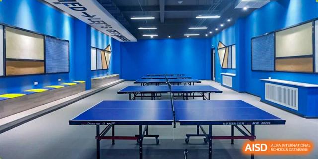 The clean and spacious table tennis hall at Oriental Cambridge International School, featuring multiple blue ping pong tables under bright ceiling lights.