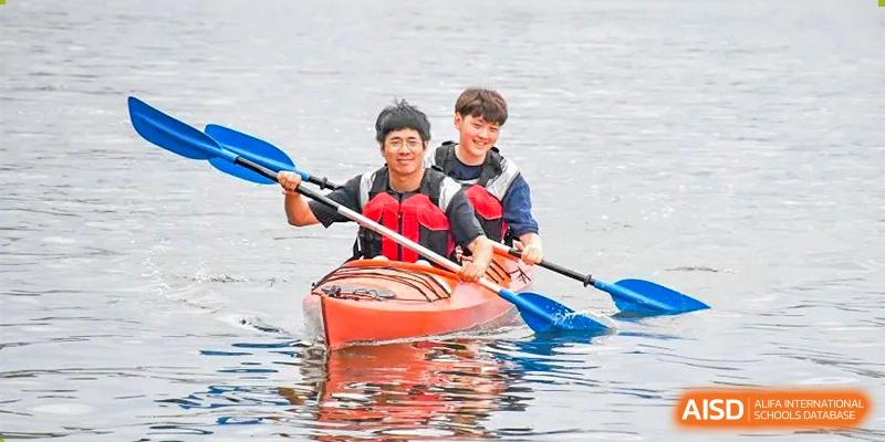 Two students from Oriental Cambridge International School smiling and paddling a red kayak on a body of water during an outdoor education activity.