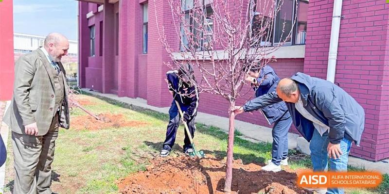 Students or staff from Oriental Cambridge International School planting a small tree with pink blossoms outside the school building as part of a campus greening initiative.