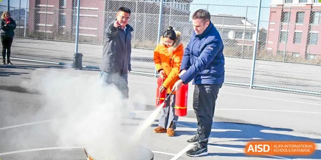 A close-up of an adult or student at Oriental Cambridge International School practicing fire safety by using a fire extinguisher to put out a fire outdoors.