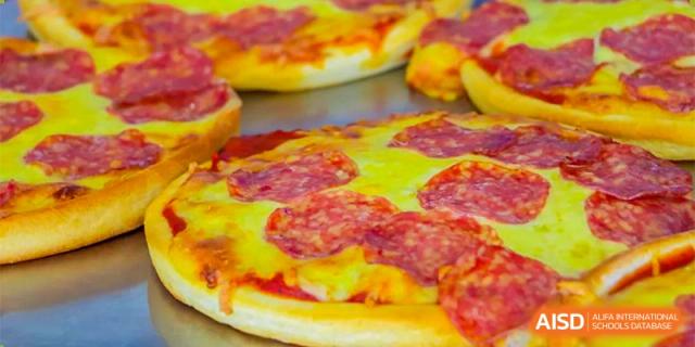 A close-up of a large, freshly baked pepperoni pizza slice, one of the meal options at Oriental Cambridge International School.